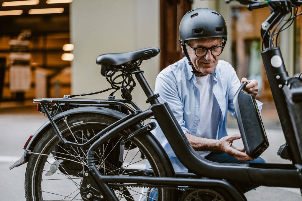 Man sitter på huk intill en elcykel.