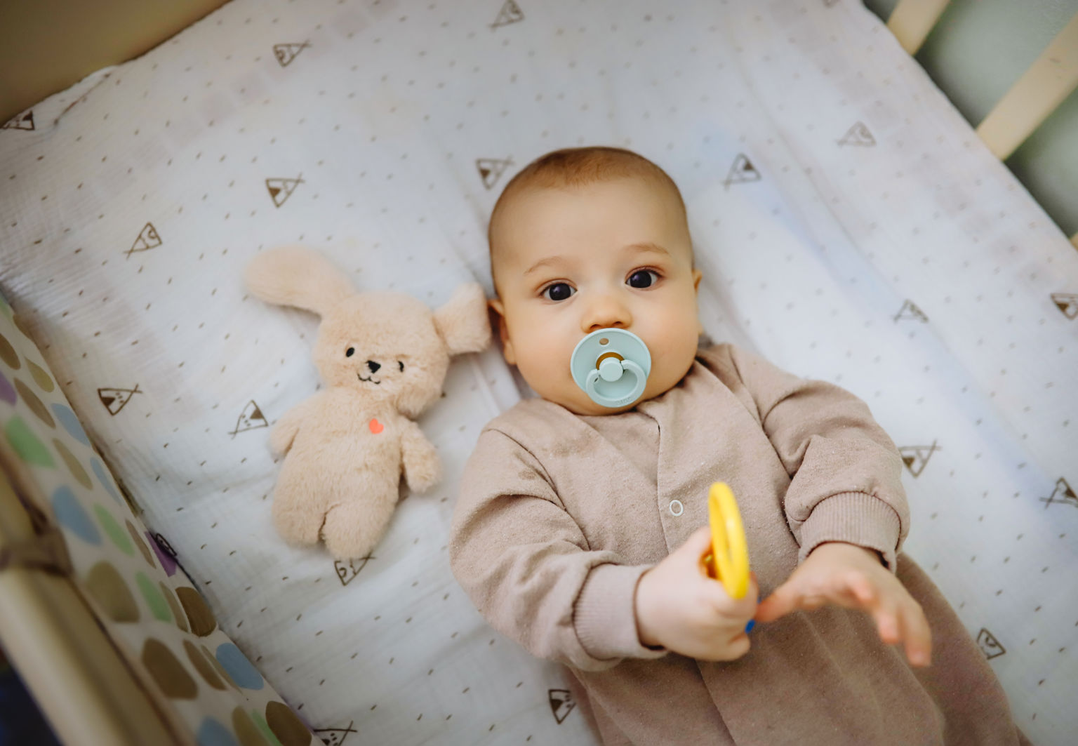 Bebis ligger vaken i en spjälsäng med napp i munnen