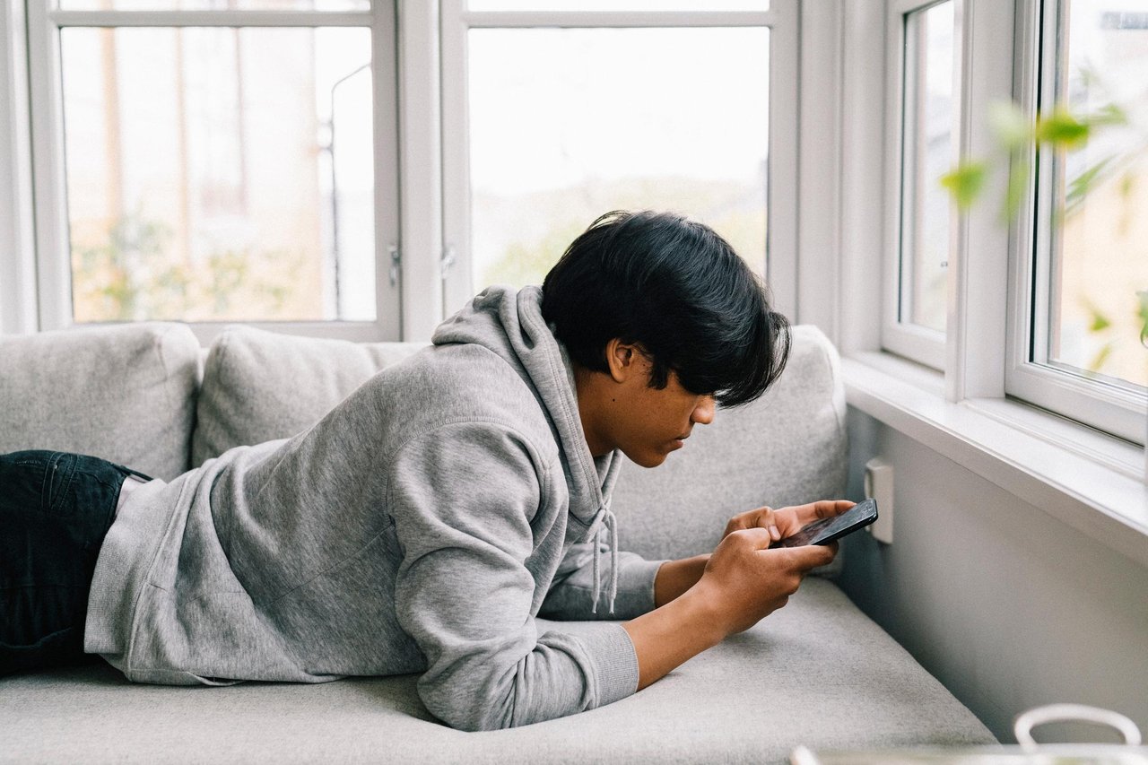 Tonårskille ligger i soffan och surfar på sin mobiltelefon