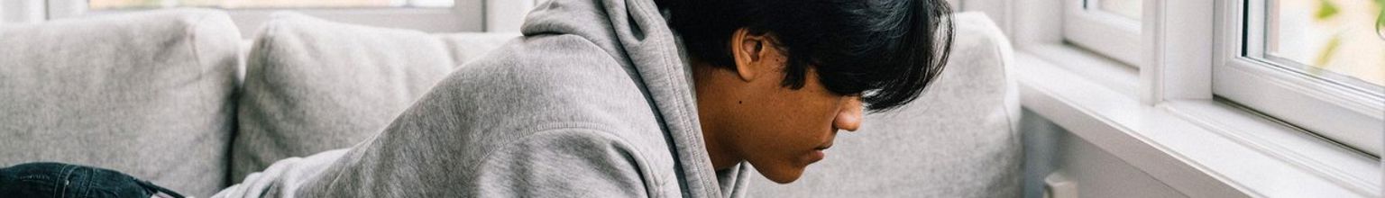 Tonårskille ligger i soffan och surfar på sin mobiltelefon