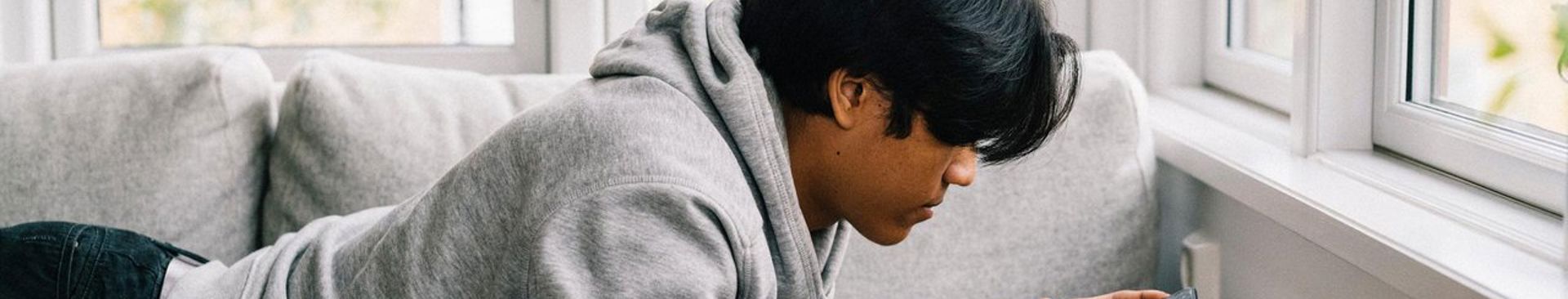 Tonårskille ligger i soffan och surfar på sin mobiltelefon