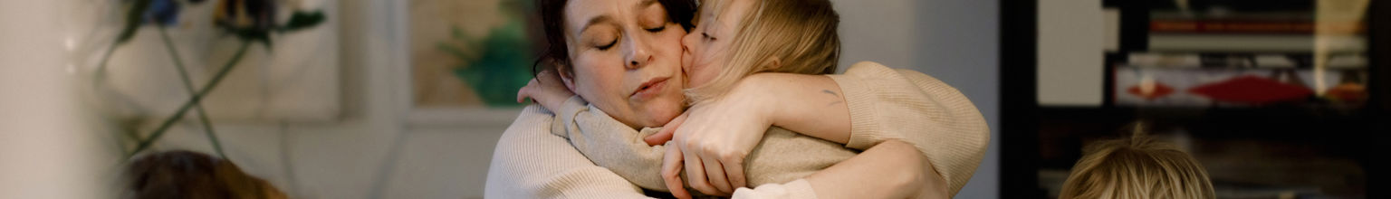 Mamma kramar om sitt barn vid ett bord där övriga pysslar med papper och penna