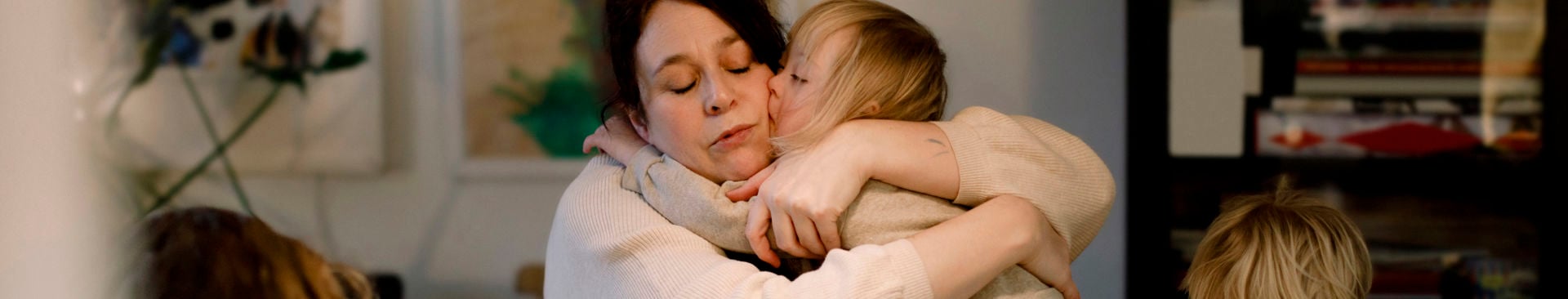 Mamma kramar om sitt barn vid ett bord där övriga pysslar med papper och penna