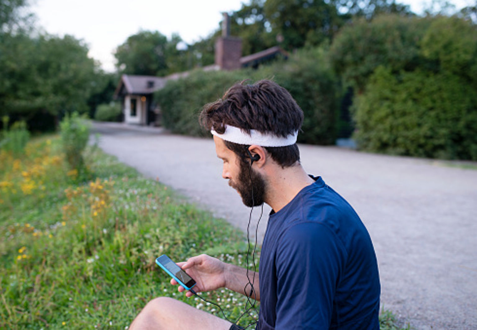 Man med löparkläder sitter med telefonen vid vägkanten efter ett träningspass