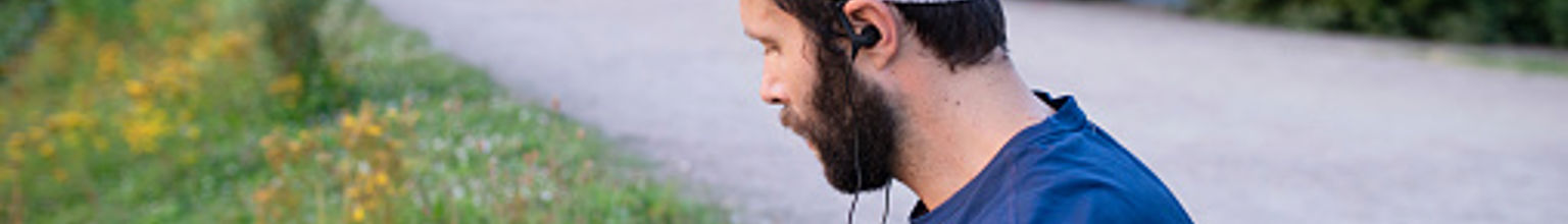 Man med löparkläder sitter med telefonen vid vägkanten efter ett träningspass