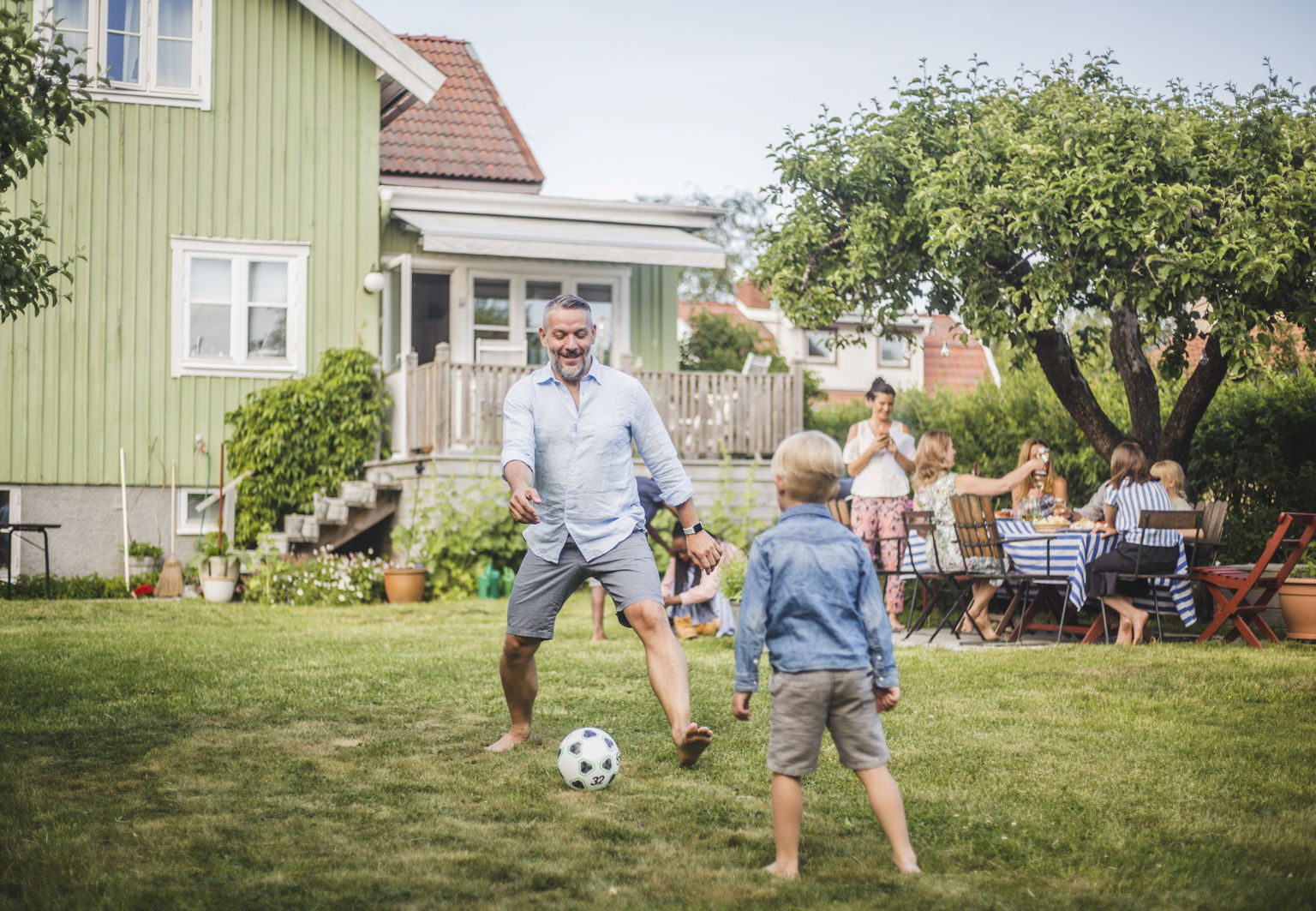 Pappa och pojke spelar fotboll på tomten utanför ett hus