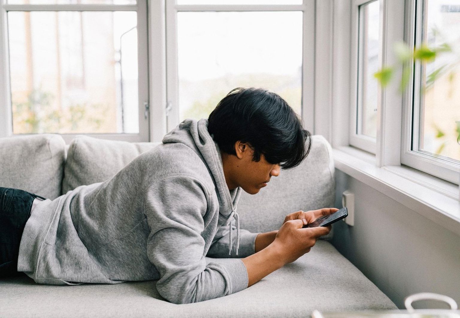 Tonårskille ligger i soffan och surfar på sin mobiltelefon