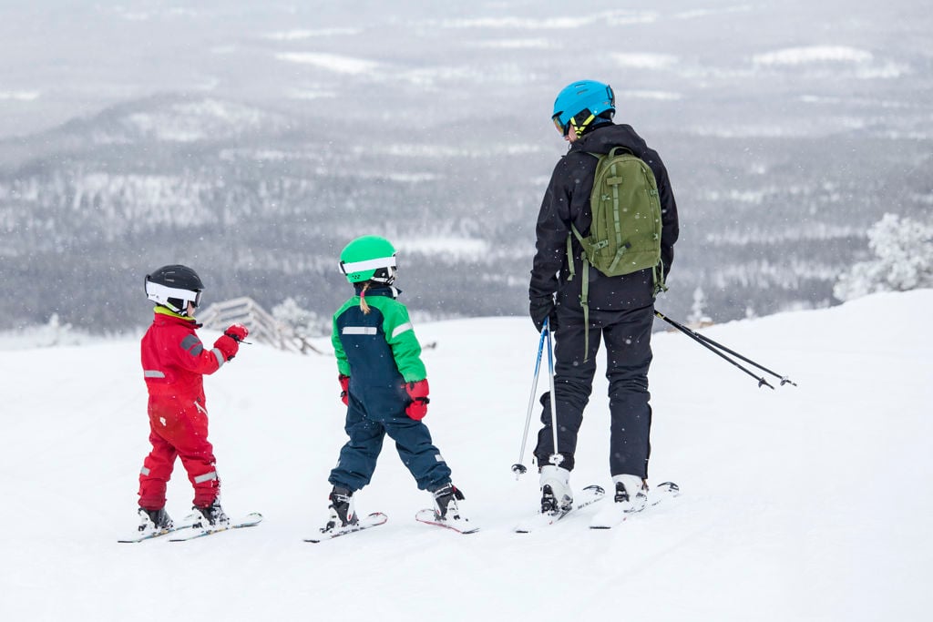 En vuxen och två barn i skidbacken